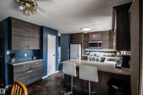 Kitchen featuring wood-finish cabinetry, a white subway tile backsplash, a built-in microwave, and a breakfast bar with stone-finish countertops - 5017 55 Ave, St. Paul Town, AB - Indoor