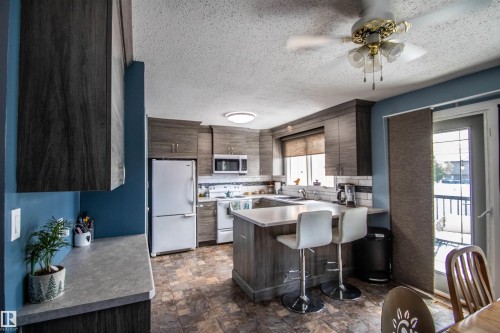 Kitchen featuring wood-finish cabinetry, white appliances, and a central island with countertop seating - 5017 55 Ave, St. Paul Town, AB - Indoor