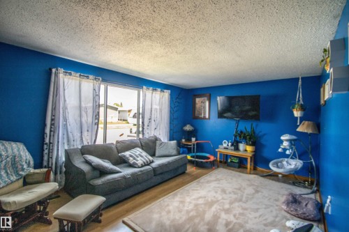 Living area featuring wood-finish flooring, a textured ceiling, and a large sliding glass door - 5017 55 Ave, St. Paul Town, AB - Indoor Photo Showing Living Room