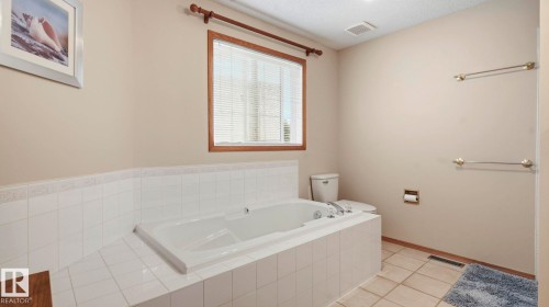 Soaking tub with white ceramic tile surround and chrome fixtures, illuminated by a window with wood trim - 125 Dechene Road Nw, Edmonton, AB - Indoor Photo Showing Bathroom
