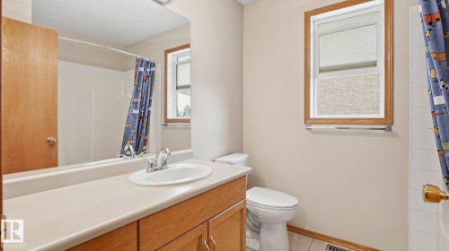 Bathroom featuring a wood-finish vanity with an integrated sink, a large wall-mounted mirror, a white toilet, and a window with wood-finish trim - 125 Dechene Road Nw, Edmonton, AB - Indoor Photo Showing Bathroom