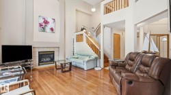 Vaulted ceilings highlight the living area, featuring wood-finish flooring and a tiled fireplace - 
