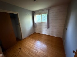 Hardwood flooring with a natural finish, featuring a window with natural light, a wood-paneled accent wall, and a recessed closet space - 