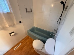 Bathroom featuring wood-finish flooring, a blue tub, white tiled shower surround, and a white toilet - 