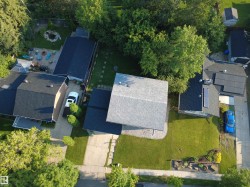 Aerial property view featuring a light grey shingle roof, paved driveway, mature trees, manicured lawns, and established landscaping - 