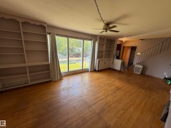 Living area featuring wood-finish flooring, built-in shelving units, a ceiling fan fixture, and expansive picture windows - 