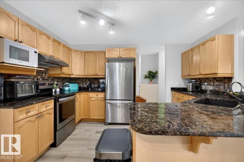 Kitchen featuring wood cabinetry, dark speckled countertops, and a mosaic tile backsplash - 6 Norfolk Close, St. Albert, AB - Indoor Photo Showing Kitchen