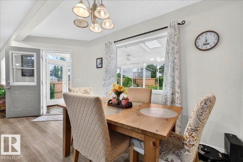 Dining area featuring wood-finish flooring, a contemporary chandelier, and a large window overlooking a sunroom - 6 Norfolk Close, St. Albert, AB - Indoor Photo Showing Dining Room