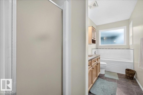 Full bathroom featuring a shower enclosure with frosted glass, a large vanity with light wood cabinetry and a stone-look countertop, a built-in bathtub with a tiled surround, a toilet, and a window providing natural light - 6 Norfolk Close, St. Albert, AB - Indoor Photo Showing Bathroom