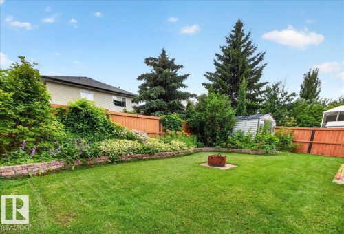 Expansive lawn featuring a fire pit, mature perimeter trees, and a garden bed with retaining wall - 6 Norfolk Close, St. Albert, AB - Outdoor With Backyard