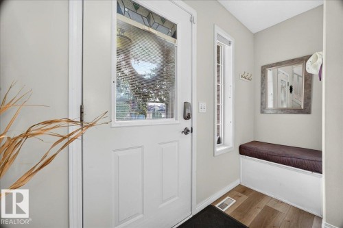 Entryway featuring a white paneled door with decorative glass, wood-finish flooring, a built-in bench with cushion, and a vertical window - 6 Norfolk Close, St. Albert, AB - Indoor Photo Showing Other Room