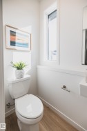 Compact powder room featuring wood-finish flooring, a contemporary window, and crisp white walls with a chair rail accent - 