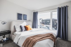 Bedroom featuring a large picture window with dark draperies, light gray carpeting, and a built-in upholstered headboard - 