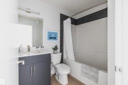 Bathroom featuring a white bathtub, gray vanity with a single sink, light wood-finish flooring, and a dark accent wall border - 
