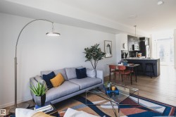 Open-concept living space featuring wood-finish flooring, a contemporary kitchen with dark cabinetry, a kitchen island with seating, a dining area, and recessed lighting - 