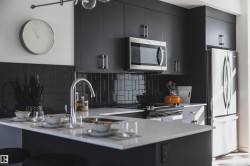 Modern kitchen featuring dark cabinetry with brushed nickel hardware, stainless steel appliances, and a white countertop island with an integrated sink - 