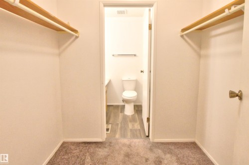 Walk-in closet with carpet flooring and ample hanging space, featuring a private water closet with wood-finish flooring - #302 47 Akins Dr, St. Albert, AB - Indoor