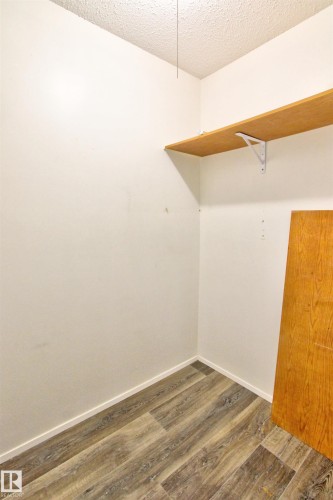 Corner closet featuring wood-finish flooring, a single wooden shelf with white brackets, white baseboards, and textured ceiling - #302 47 Akins Dr, St. Albert, AB - Indoor