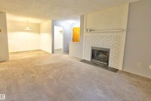 Living area featuring a white brick fireplace with a dark-toned hearth - #302 47 Akins Dr, St. Albert, AB - Indoor Photo Showing Living Room With Fireplace