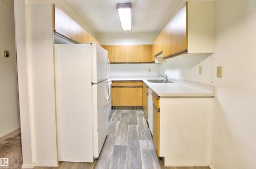 Galley kitchen featuring wood-finish cabinetry, white countertops, and wood-finish flooring - #302 47 Akins Dr, St. Albert, AB - Indoor Photo Showing Kitchen With Double Sink