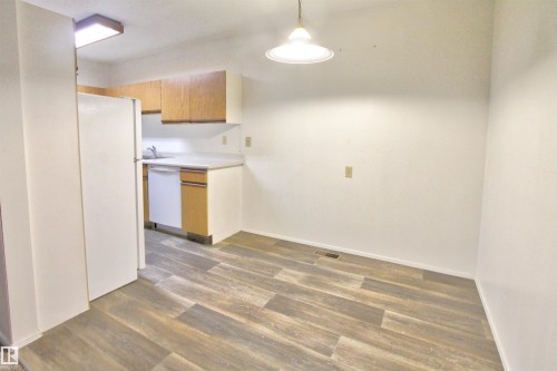 Open-concept dining area featuring wood-finish flooring, a pendant light fixture, and direct access to a kitchen with wood cabinetry - #302 47 Akins Dr, St. Albert, AB - Indoor Photo Showing Kitchen