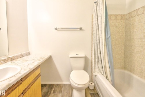 Bathroom featuring wood-finish flooring, a toilet, and a bathtub with tiled surround - #302 47 Akins Dr, St. Albert, AB - Indoor Photo Showing Bathroom