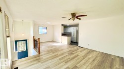 Open-concept living space featuring wood-finish flooring, a ceiling fan, and a kitchen visible in the background - 
