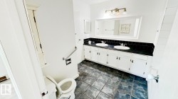 Bathroom featuring a dual vanity with white cabinetry, a dark countertop, and black tile backsplash - 