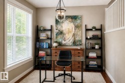 Dedicated office space featuring hardwood flooring, a large window with white blinds, a tiered chandelier, and built-in shelving - 