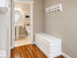 Hardwood flooring in a hallway leading to a bathroom featuring a pedestal sink, round mirror, and wall-mounted lighting fixture - 