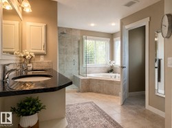 Bathroom featuring a dual vanity with dark countertops, a large soaking tub, a tiled walk-in shower with a glass enclosure, and light-colored floor tiles - 