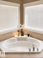 Corner soaking tub featuring chrome fixtures, integrated jets, and a tiled surround - 