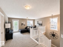 Carpeted bonus room featuring a white railing staircase, multiple windows with blinds, a glass-paneled door, and a geometric chandelier - 