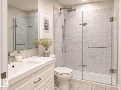 Contemporary bathroom featuring a glass-enclosed shower with tile surround, white vanity with integrated sink, and large wall-mounted mirror - 