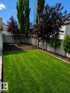 Fenced backyard featuring a manicured lawn, established trees, and a decorative fountain - 