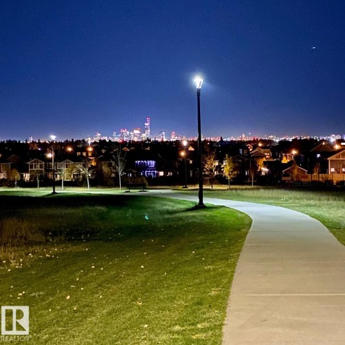 Paved pathway through green space, featuring a street light and distant city skyline - 2337 Frezenberg Avenue Nw, Edmonton, AB - Outdoor With View