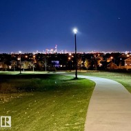 Paved pathway through green space, featuring a street light and distant city skyline - 