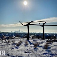 Outdoor area featuring a contemporary pergola structure and multiple park benches, all set against a distant cityscape - 