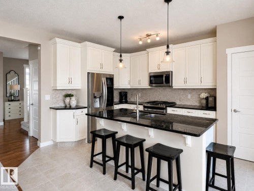 Kitchen featuring cream-colored cabinetry, black countertops, stainless steel appliances, and a tiled backsplash - 2337 Frezenberg Avenue Nw, Edmonton, AB - Indoor Photo Showing Kitchen With Upgraded Kitchen