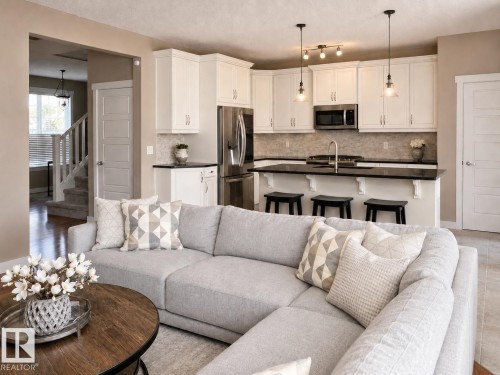Open-concept living space featuring a modern kitchen with white cabinetry, stainless steel appliances, a dark countertop, and a tiled backsplash - 2337 Frezenberg Avenue Nw, Edmonton, AB - Indoor