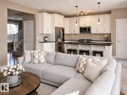 Open-concept living space featuring a modern kitchen with white cabinetry, stainless steel appliances, a dark countertop, and a tiled backsplash - 