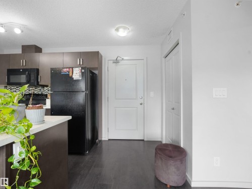 Modern kitchen featuring dark wood-finish cabinetry, a black appliance suite, and a mosaic tile backsplash - #422 5515 7 Av Sw, Edmonton, AB - Indoor Photo Showing Kitchen