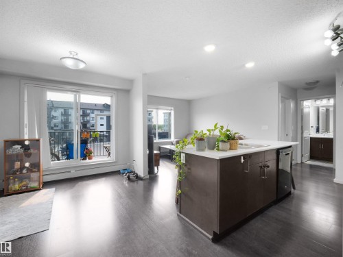 Open-concept living space featuring wood-finish flooring, a kitchen island with integrated sink and dishwasher, and a sliding glass door opening to a balcony - #422 5515 7 Av Sw, Edmonton, AB - Indoor