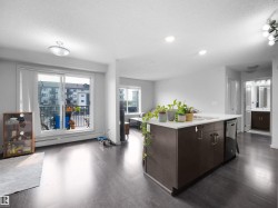 Open-concept living space featuring wood-finish flooring, a kitchen island with integrated sink and dishwasher, and a sliding glass door opening to a balcony - 