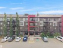 Contemporary multi-story building featuring a facade of grey and brown panels, accented with a vibrant red central section - #422 5515 7 Av Sw, Edmonton, AB  - Outdoor With Facade 