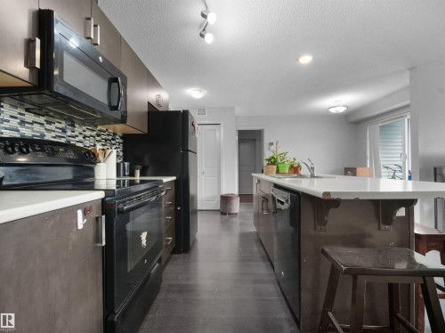 Modern kitchen featuring dark wood-finish cabinetry, white countertops, and a mosaic tile backsplash - #422 5515 7 Av Sw, Edmonton, AB - Indoor Photo Showing Kitchen