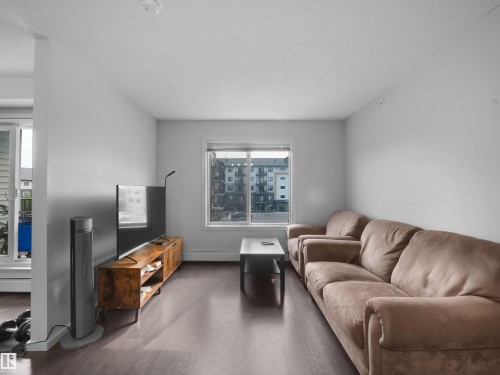 Living area featuring dark wood-finish flooring, light-toned walls, and a window with white trim - #422 5515 7 Av Sw, Edmonton, AB - Indoor Photo Showing Living Room