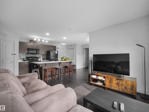 Open-concept living space featuring wood-finish flooring, a kitchen island with seating, dark cabinetry, and a mosaic tile backsplash - #422 5515 7 Av Sw, Edmonton, AB - Indoor Photo Showing Living Room