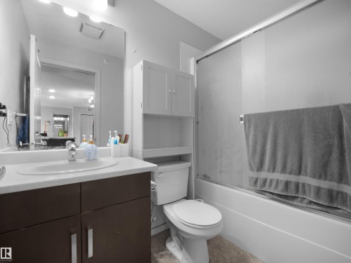 Bathroom featuring a white bathtub with a sliding glass door, a toilet, and a vanity with a white countertop - #422 5515 7 Av Sw, Edmonton, AB - Indoor Photo Showing Bathroom