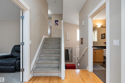 Hardwood flooring in main corridor, carpeted staircase with white railings, and a lower-level bathroom featuring wood cabinetry and a dark countertop - 16748 118 Street Nw, Edmonton, AB - Indoor Photo Showing Other Room